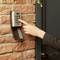 A hand pressing a button on an electronic door lock on a brick wall.