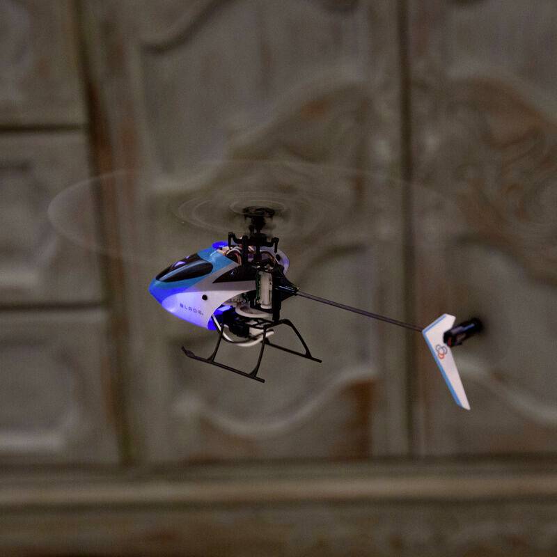 A small remote-controlled helicopter model is flying in a room. It has a blue and white paintwork with visible rotor blades.
