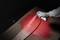 A gloved hand sprays red paint from an aerosol can onto a skateboard deck lying on a cardboard box.