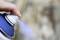 A hand sprays paint from a blue spray can. The background is out of focus.