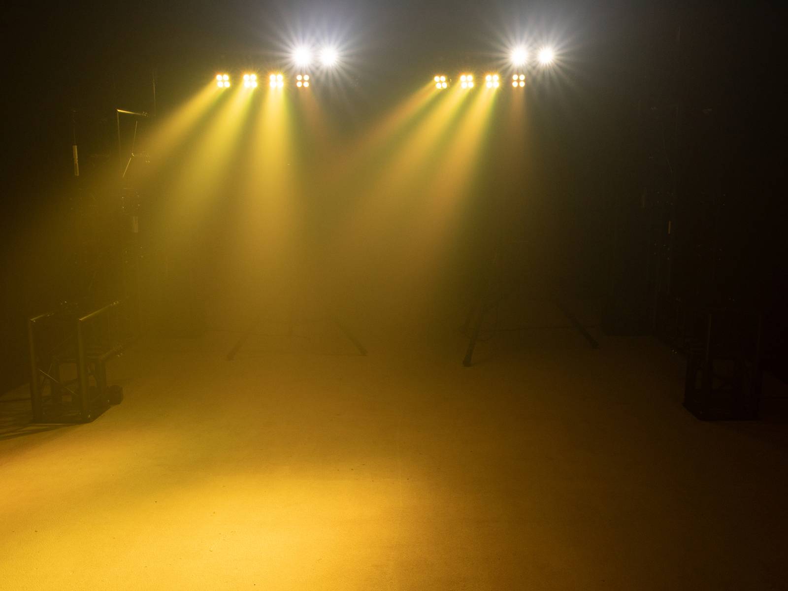 Stage bathed in yellow spotlight through misty air. Four bright lights beam down onto an empty space.