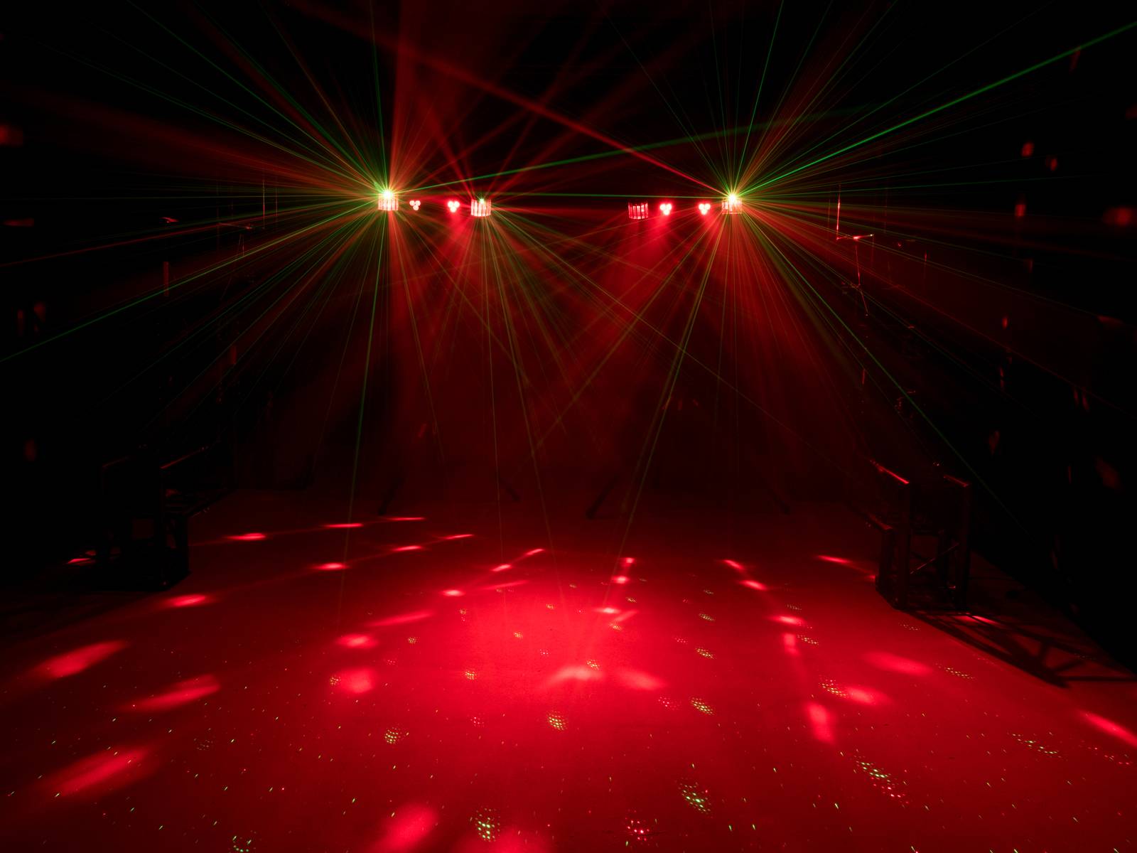 A dark stage illuminated by red spotlights and lasers radiating in different directions.