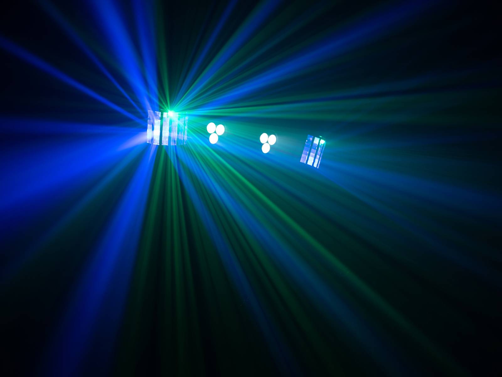 Colourful light rays stretch out across a dark room, with blue and green hues predominating. The effect of stage lighting.
