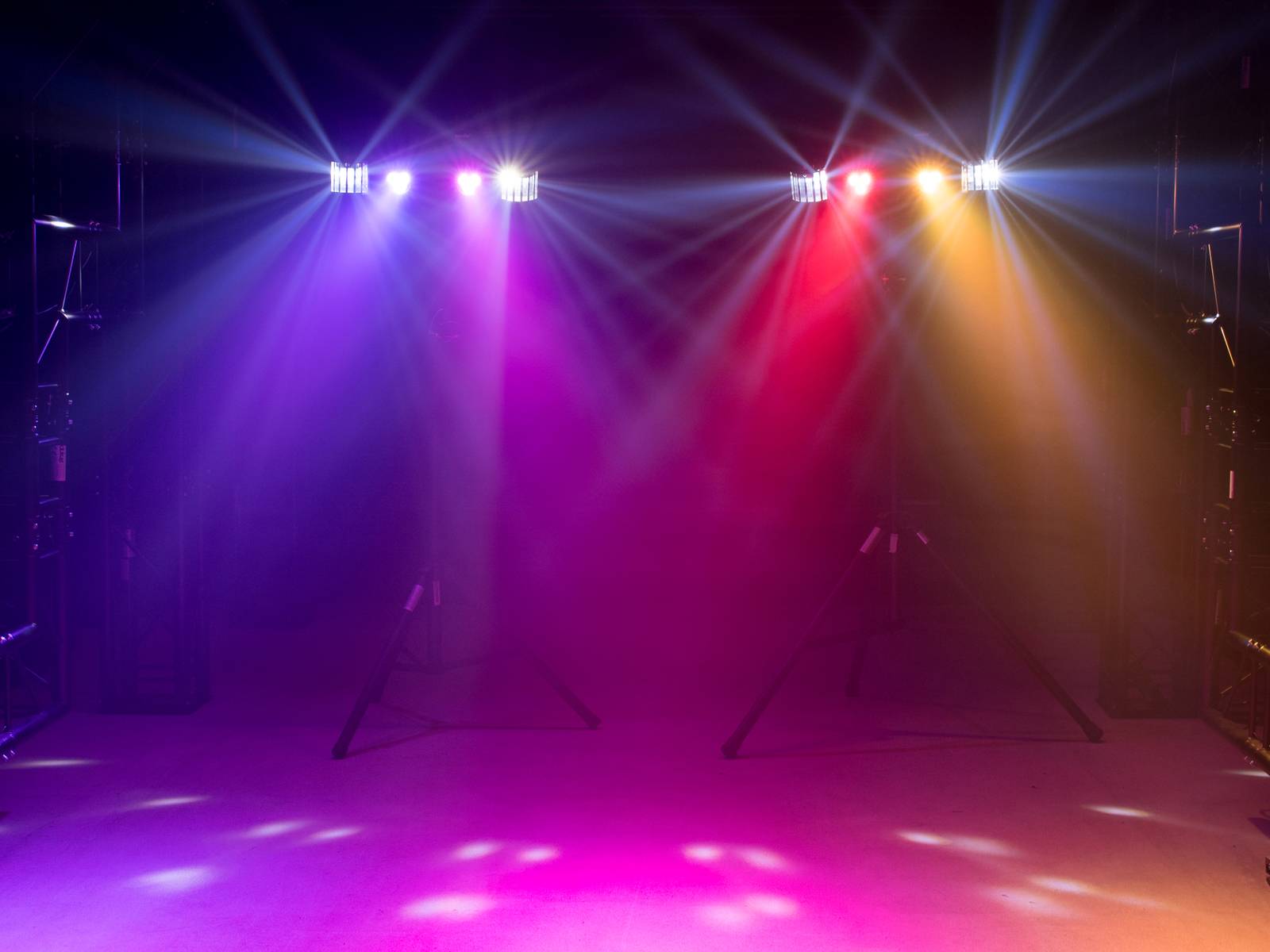 Colourful spotlights shine in blue, purple, red and yellow onto an empty stage, creating a vibrant, atmospheric ambience.