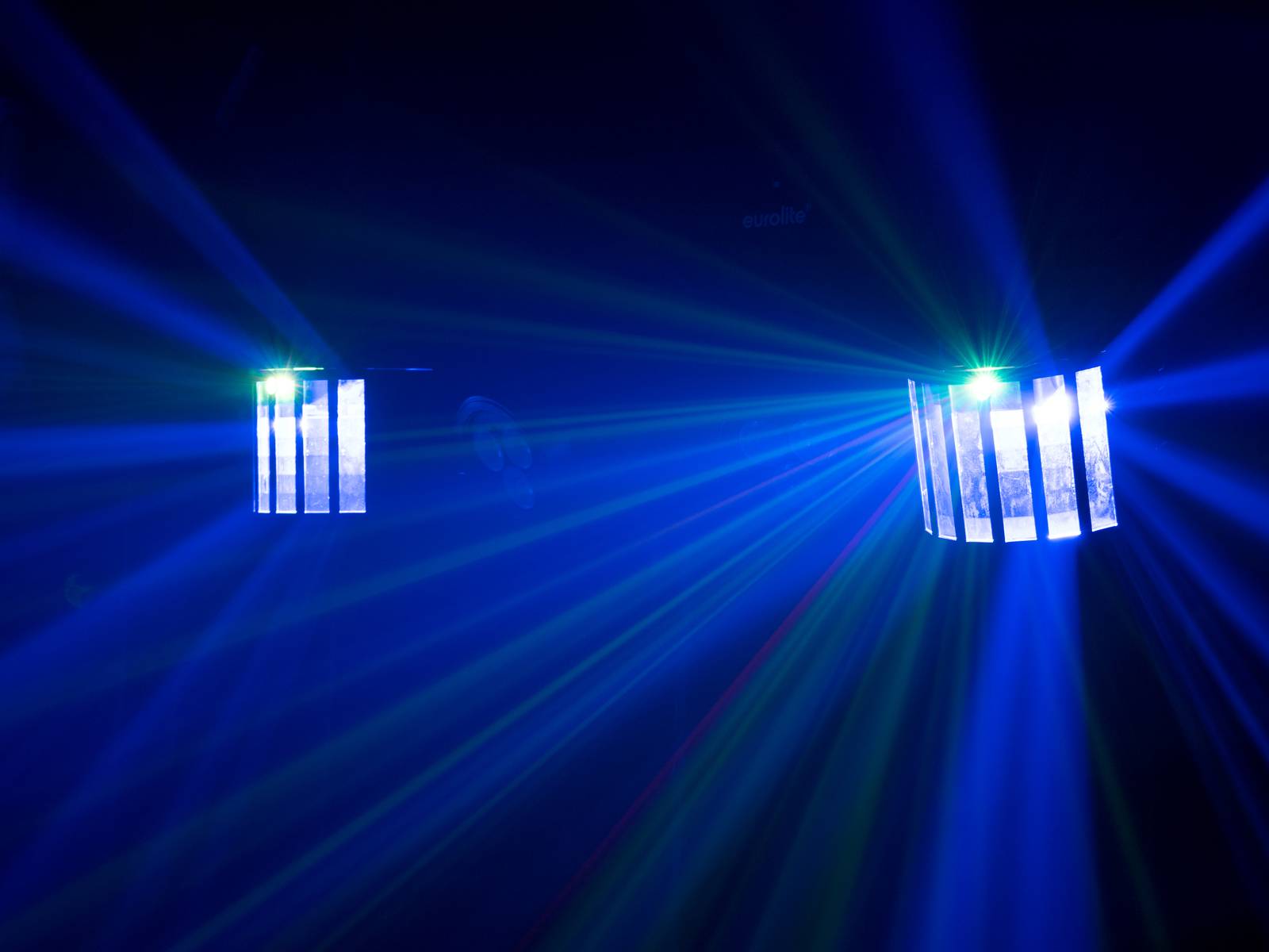 Two light projectors cast blue and green light rays in a dark room, creating a vibrant and dynamic atmosphere.