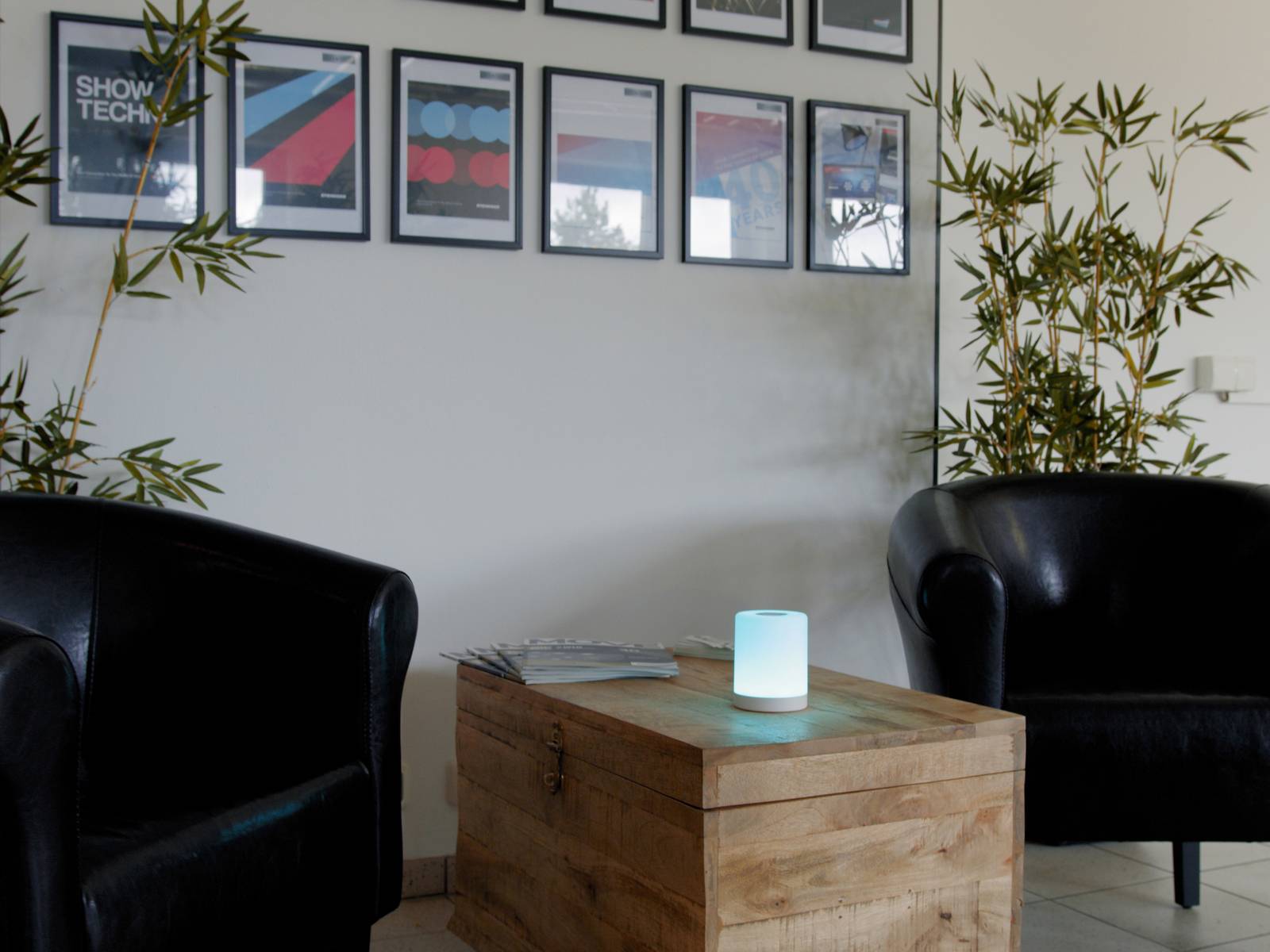 Two black armchairs surround a wooden table with a glowing, blue light. Framed pictures hang on the wall.