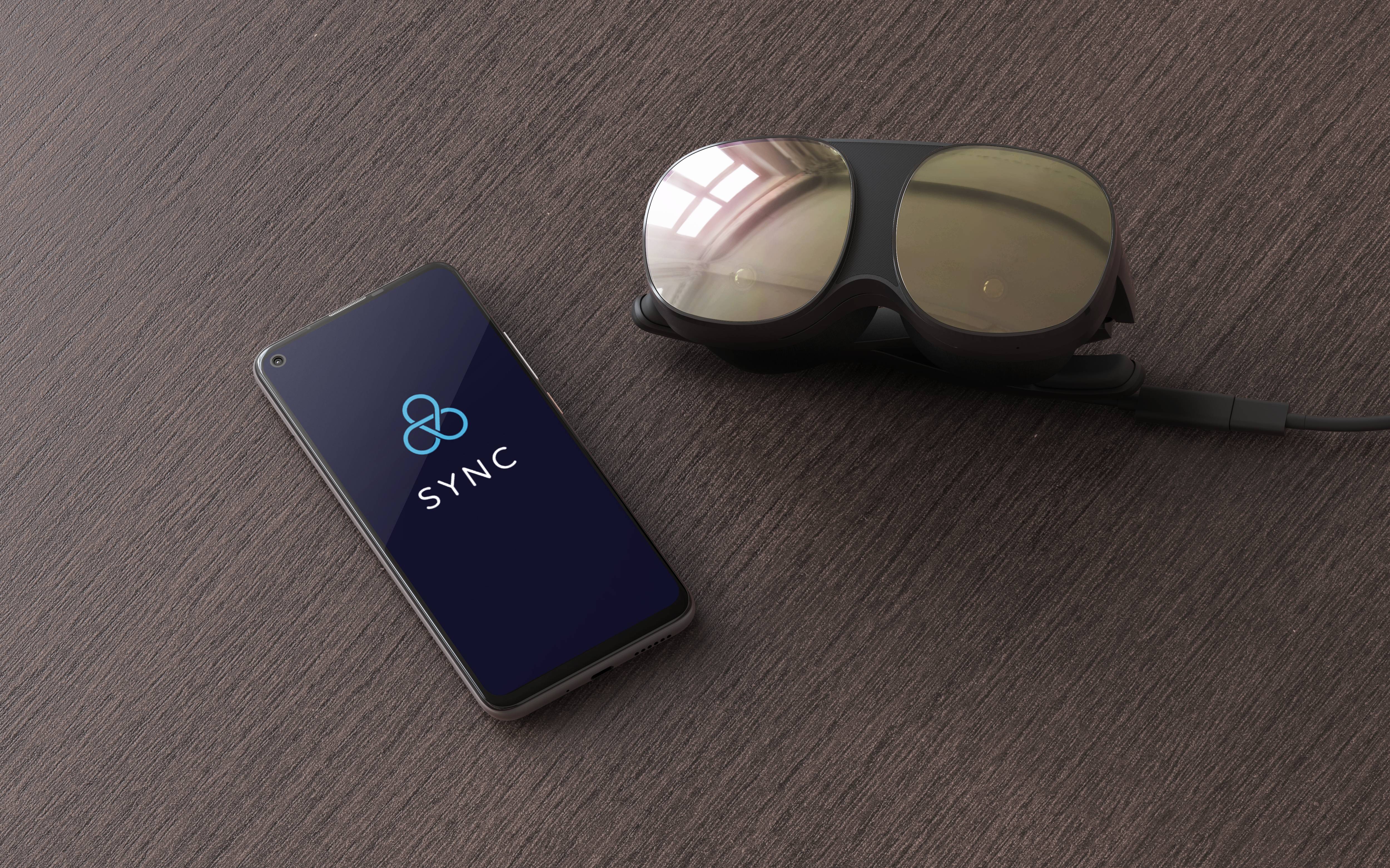 Smartphone with 'SYNC' logo on the screen next to a black VR headset on a wooden table.