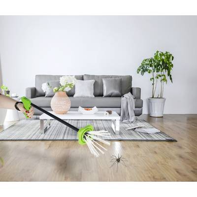 A person is using a green device to catch a spider on a wooden floor in a modernly furnished living room.
