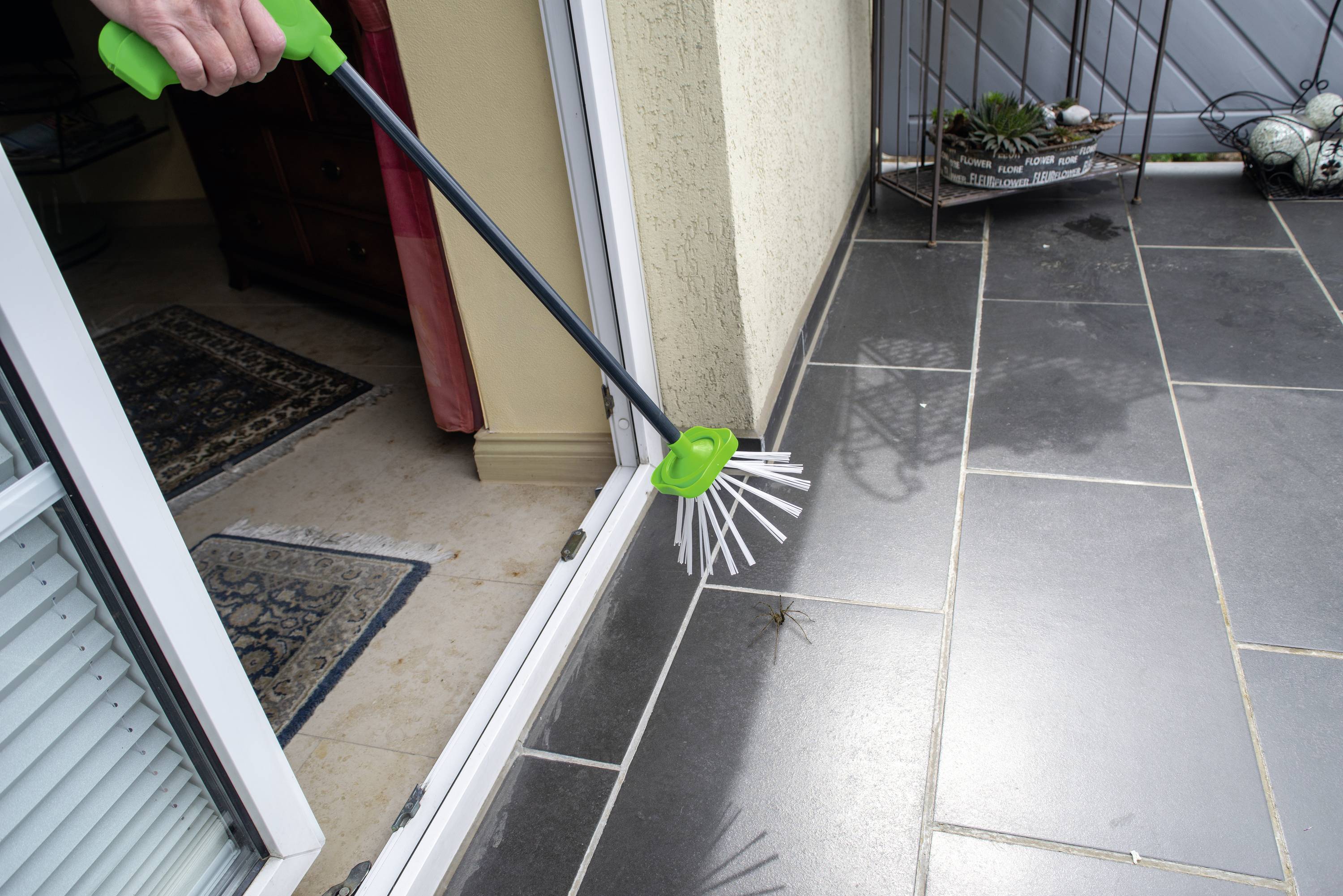 A person uses a handheld device with a grasping arm to remove an insect from a tile near a door.