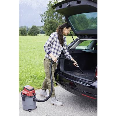 A woman is vacuuming the boot of a car. A green lawn is visible in the background.