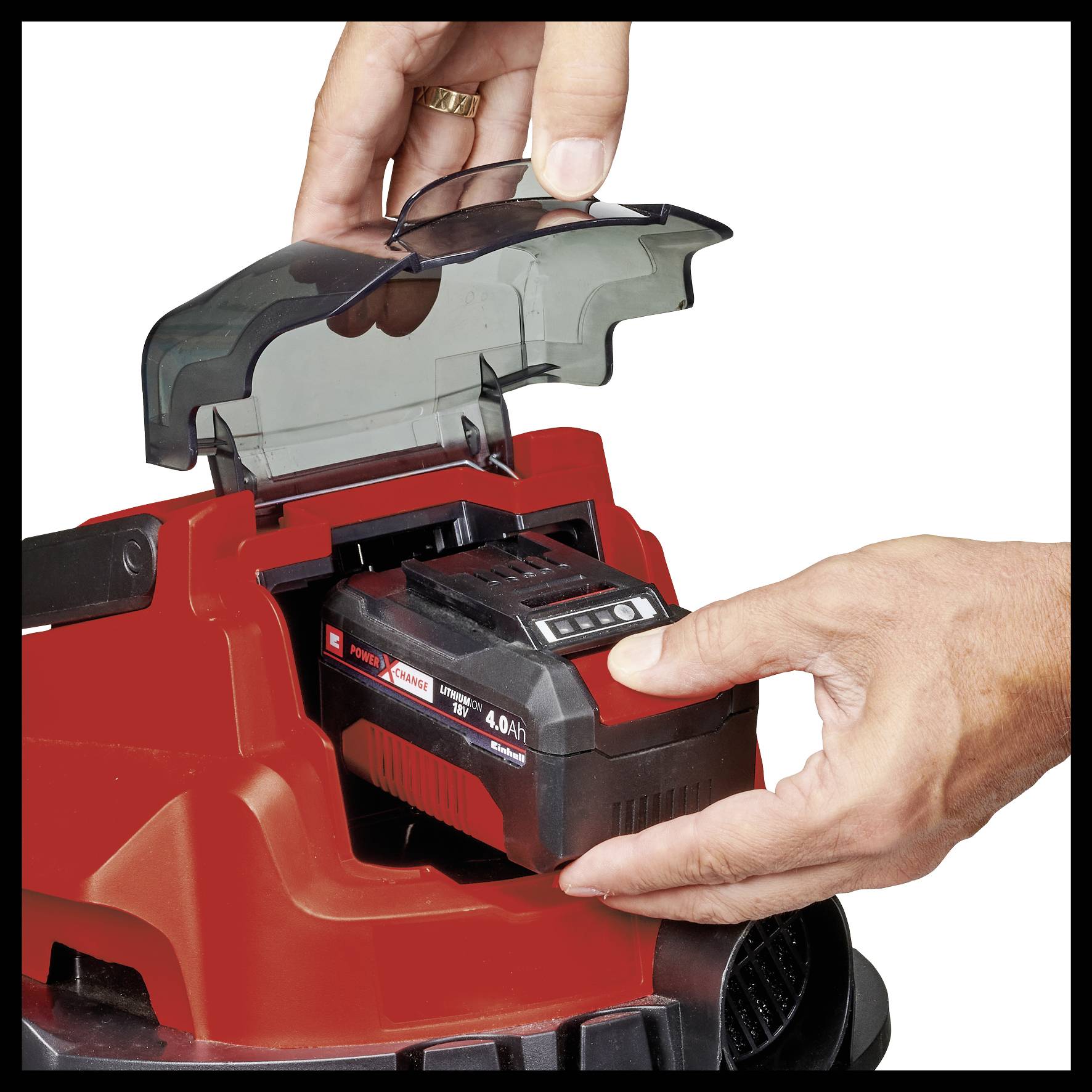 A hand is inserting a battery into a red electric tool. A transparent cover is open to allow battery insertion.