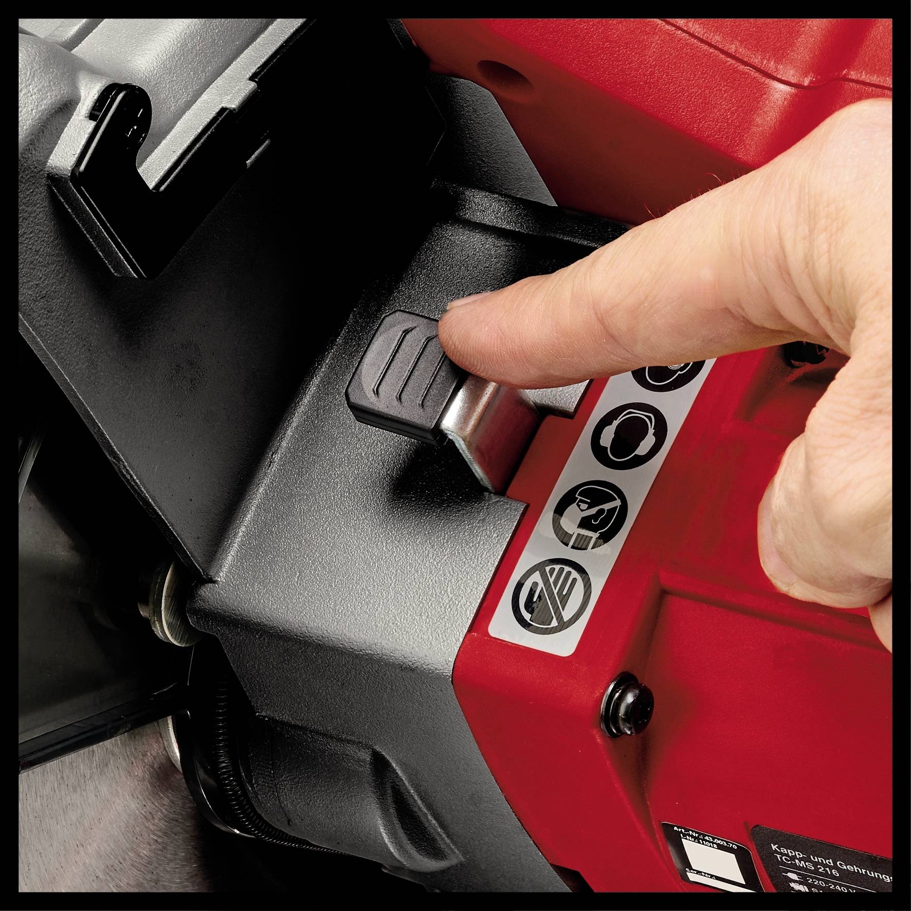 A hand presses a switch on a red device with symbols and warning notices.