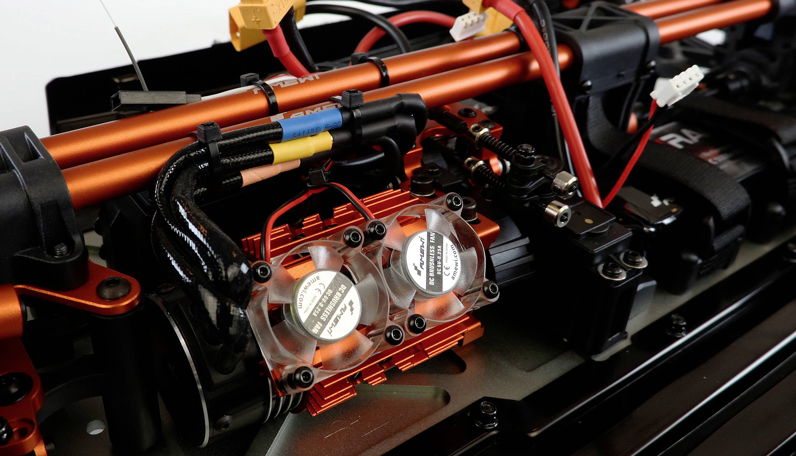 Close-up of an RC car part with multiple cables and fans. The structure is metallic with black and red components.