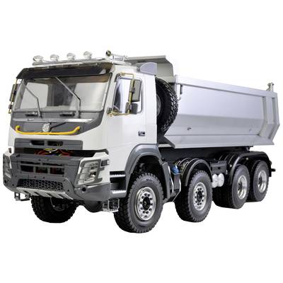 A white tipper truck with four axles is parked outside. It has a large cargo bed with spare tyres mounted on the side.