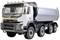 A white tipper truck with four axles is parked outside. It has a large cargo bed with spare tyres mounted on the side.