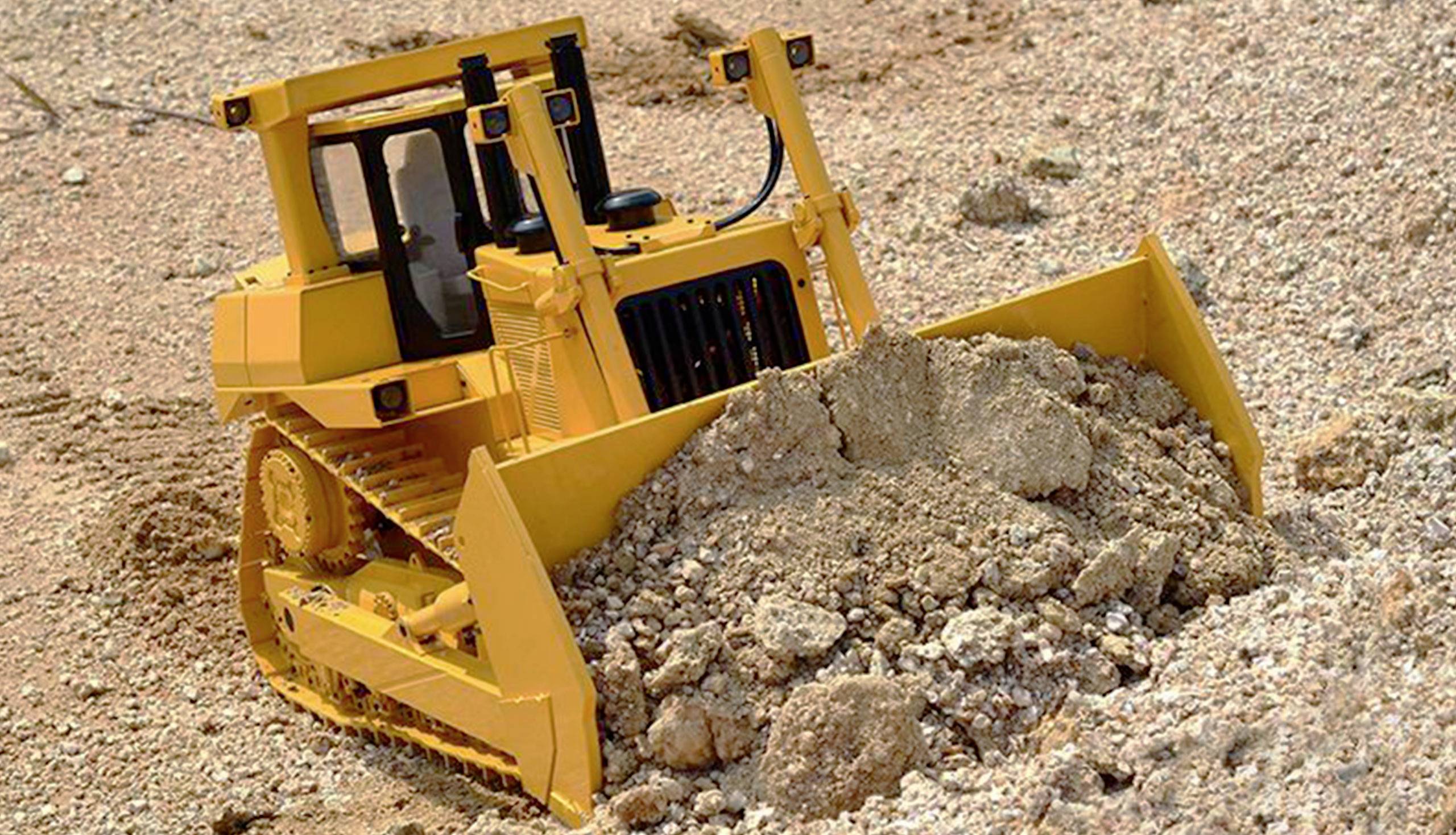 A yellow bulldozer pushes a large amount of earth in front of it across a sandy construction site.