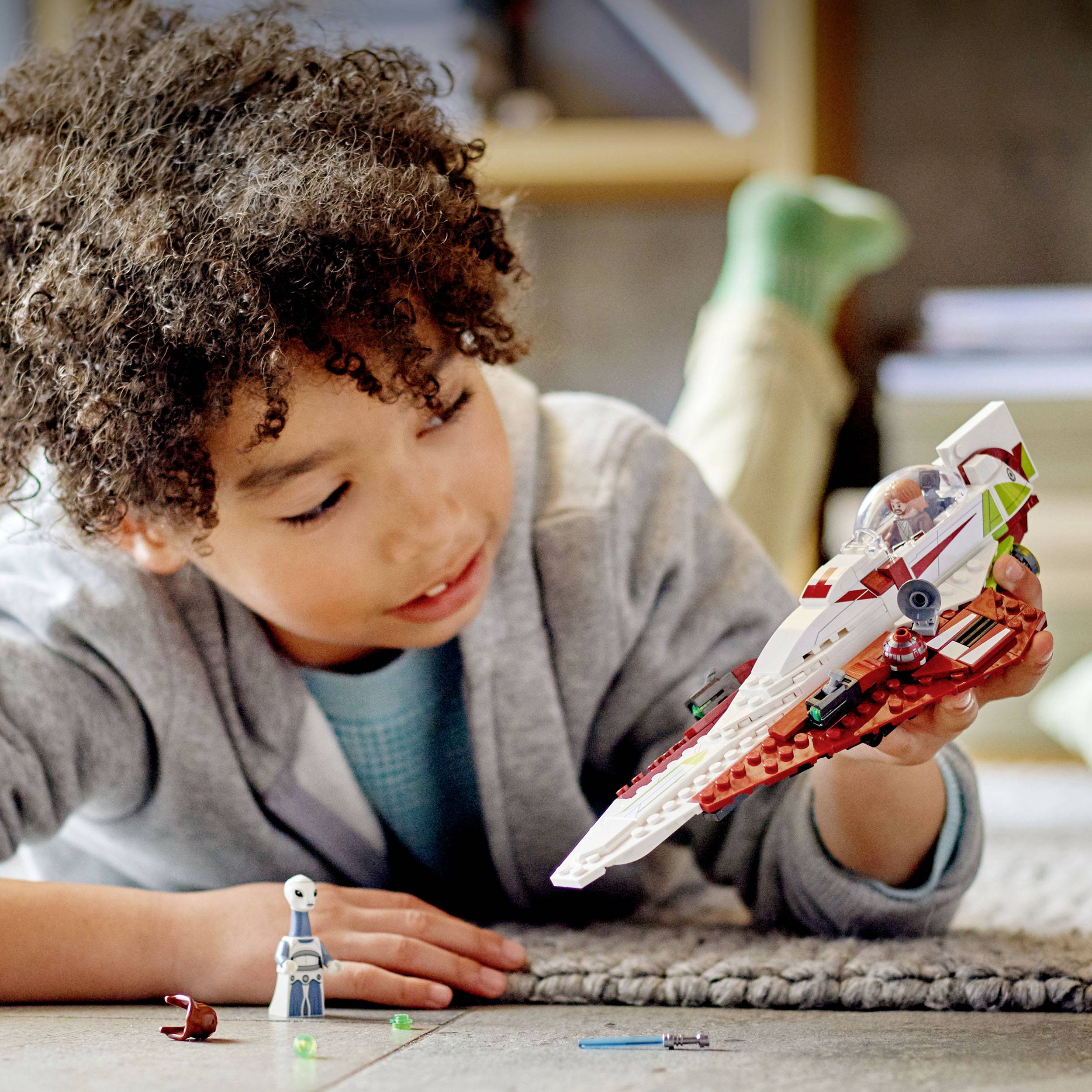 A child plays on the floor with a model spaceship and tiny figurines, focused and delighted.
