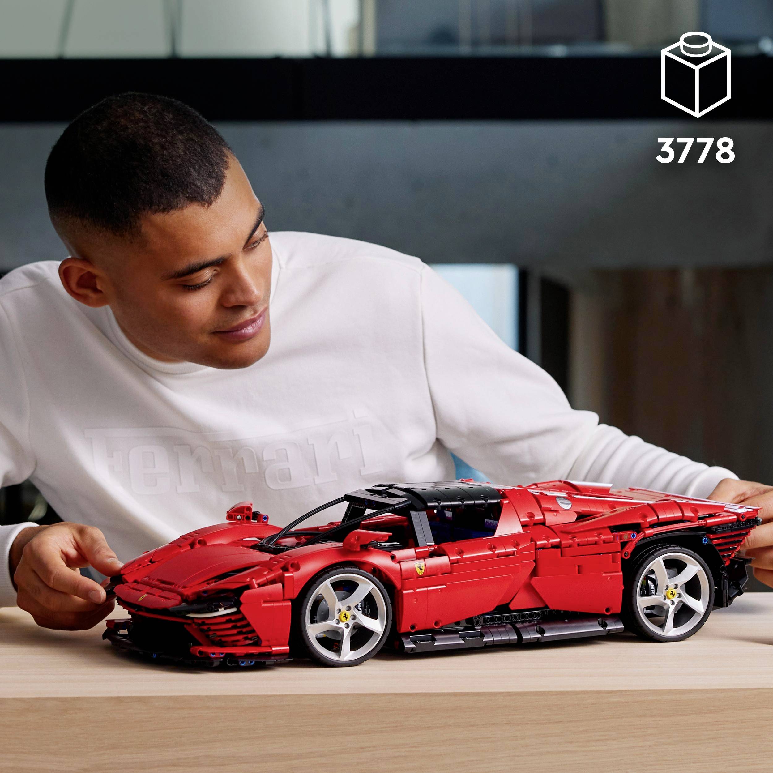 A person is examining a detailed, red toy car model that is sitting on a table in front of them.
