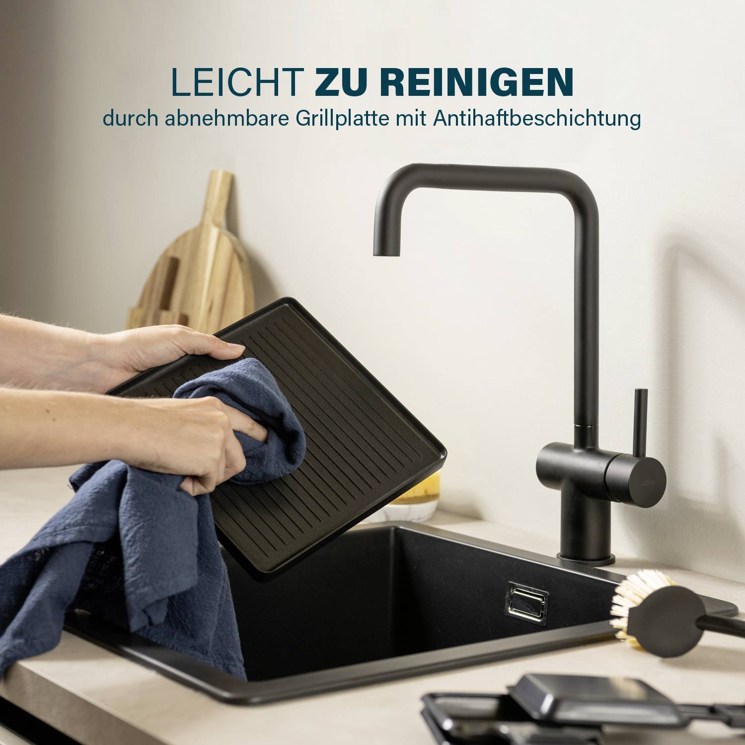 A person is cleaning a black grill plate over a sink. Text: 'Easy to clean thanks to the removable grill plate with non-stick coating.'