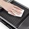A hand wipes a black griddle with a white cloth, cleaning its ridged surface.