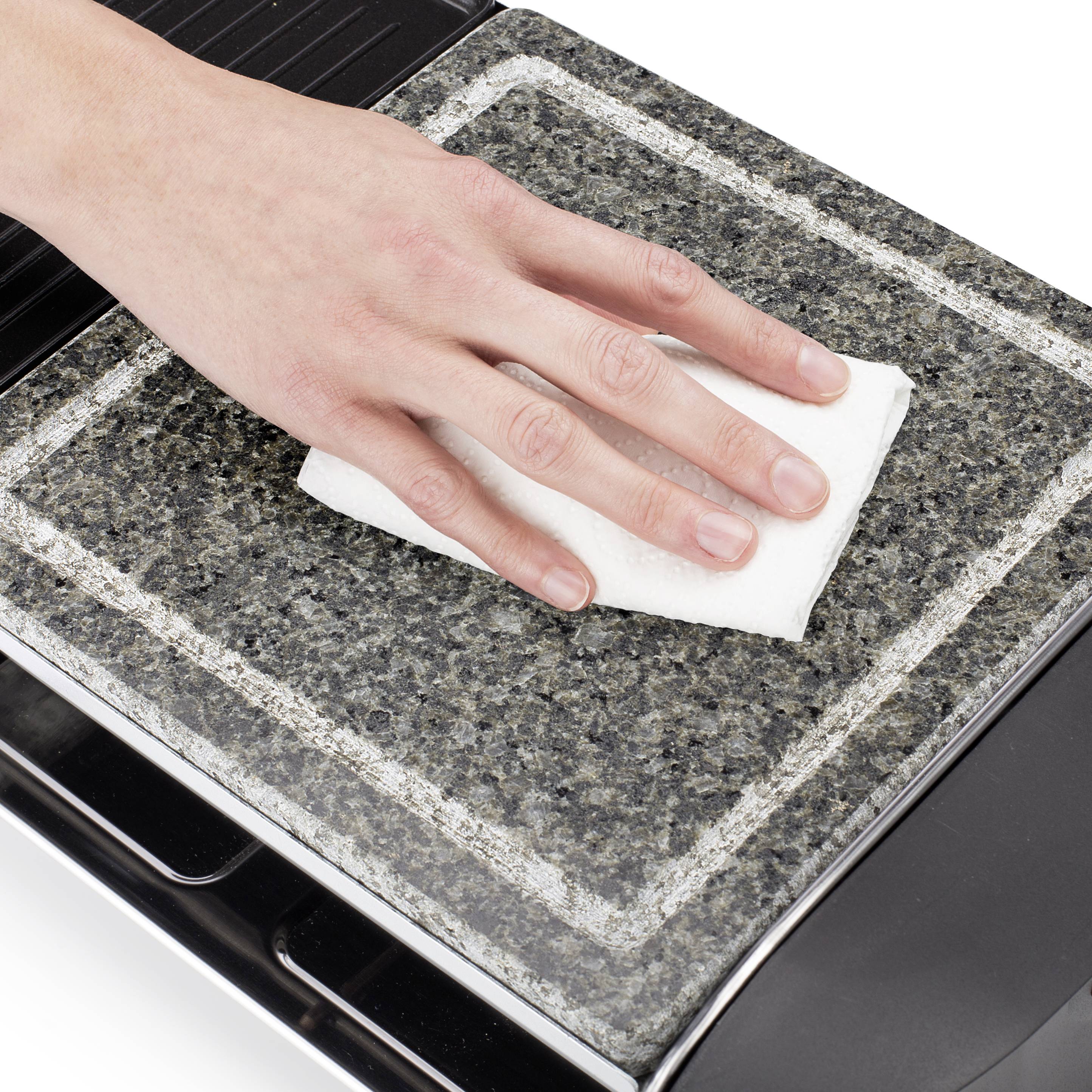 A hand wipes a dark stone surface with a white cloth, cleaning it.