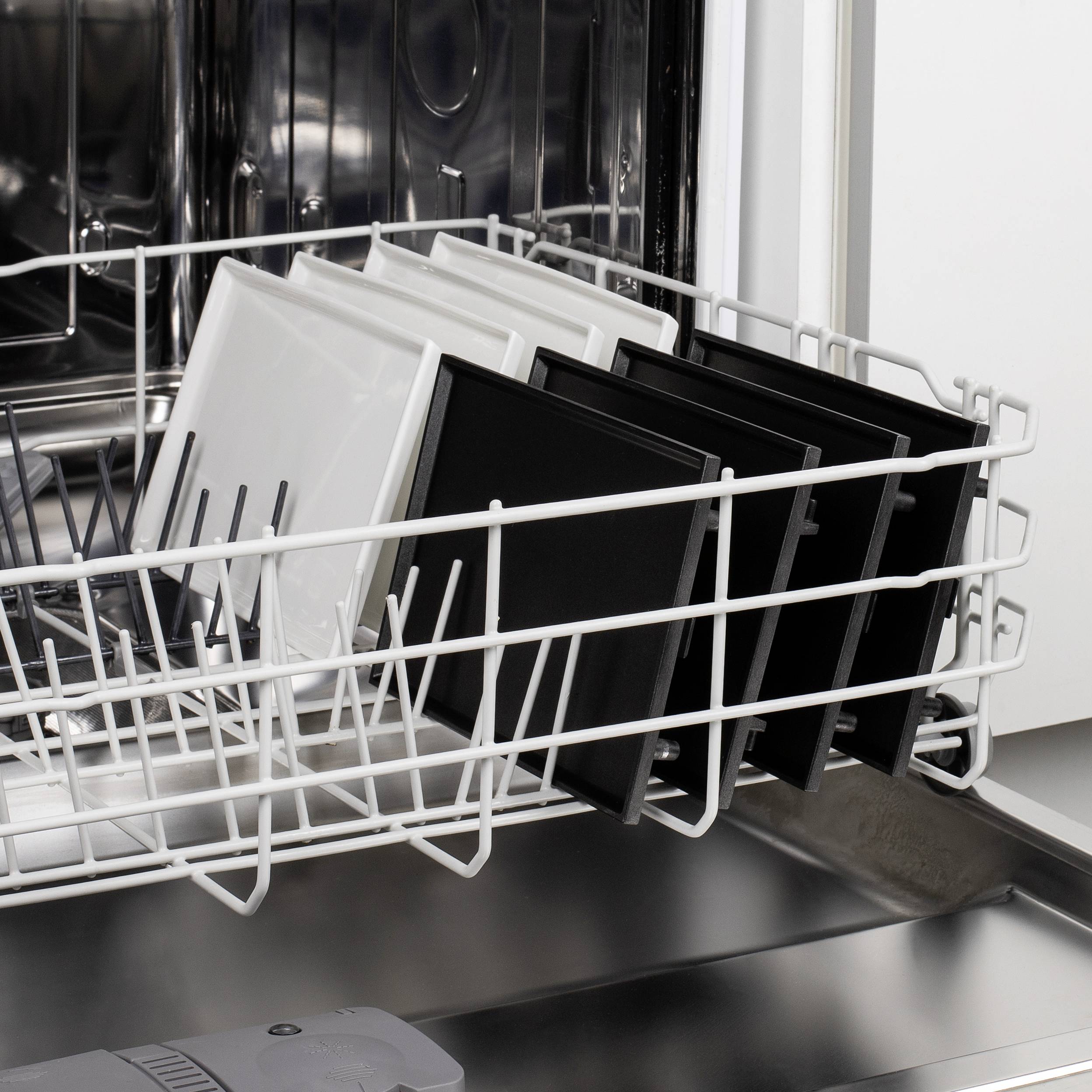 A dishwasher with an open upper rack, with several black and white plates neatly arranged in rows.