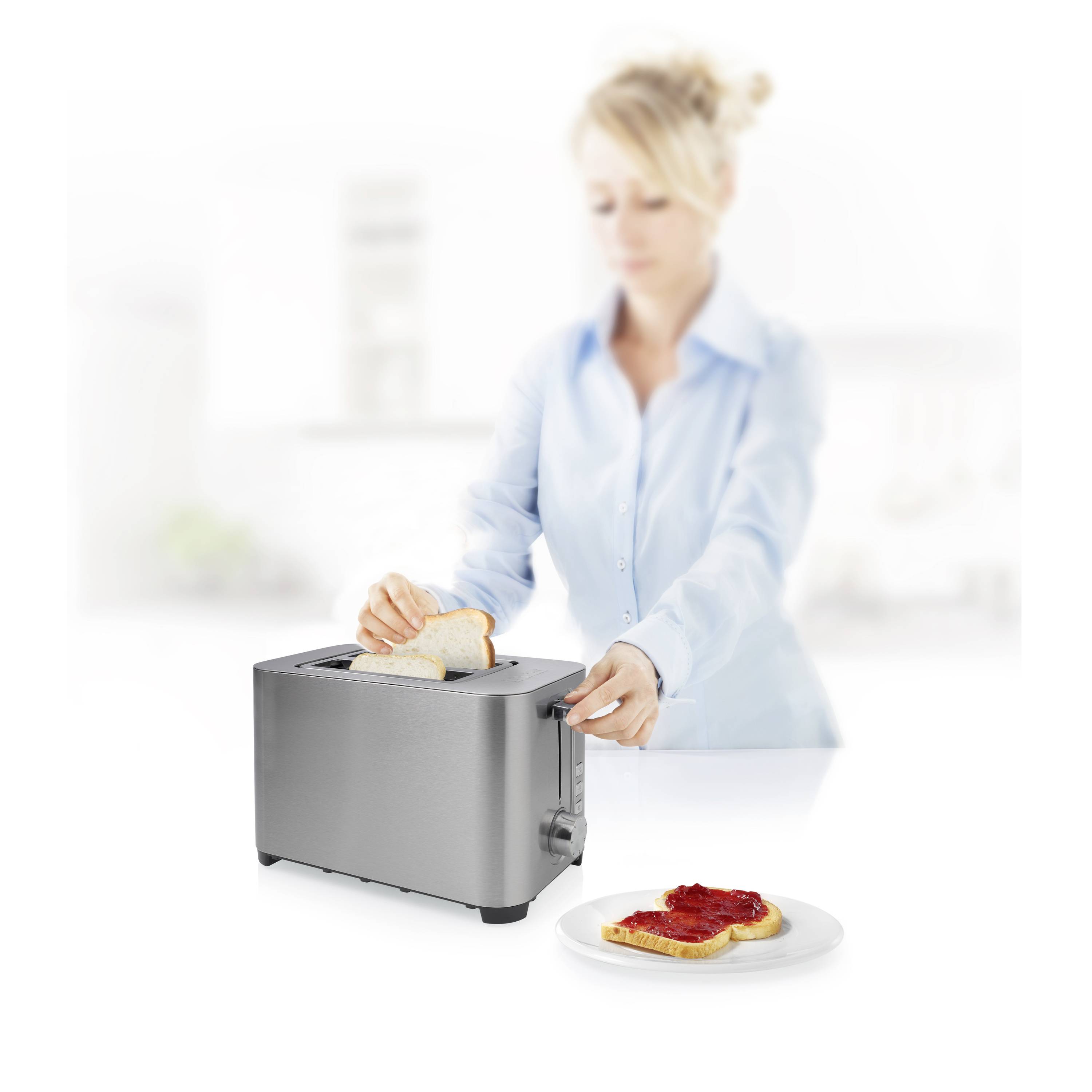 A person is preparing toast in the kitchen, with jam-covered toast beside them on a plate.