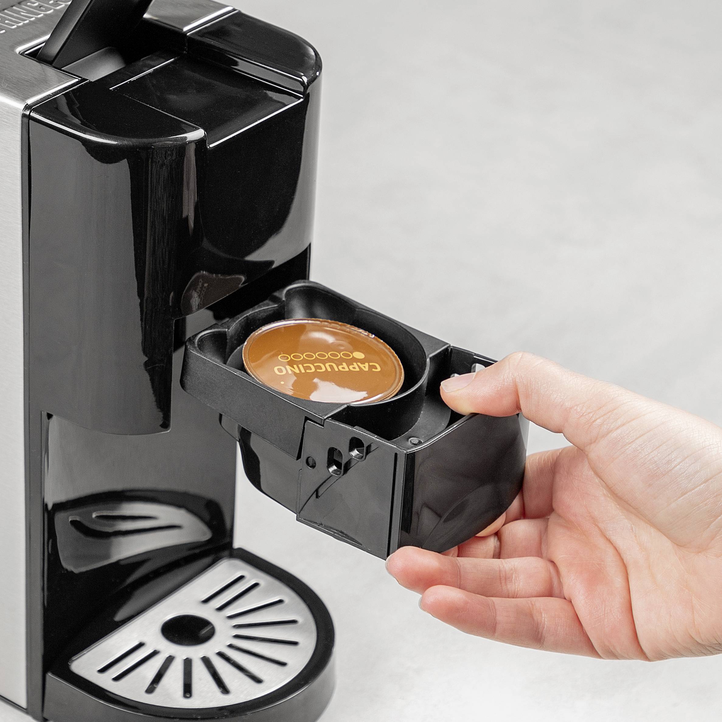 A hand places a coffee capsule into a coffee machine. The machine is black and silver with a front capsule holder.