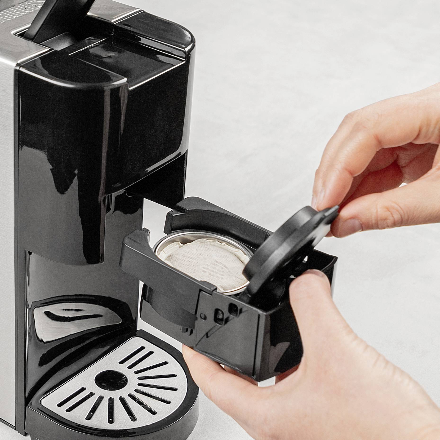 A person inserts a coffee capsule into a black capsule coffee machine.