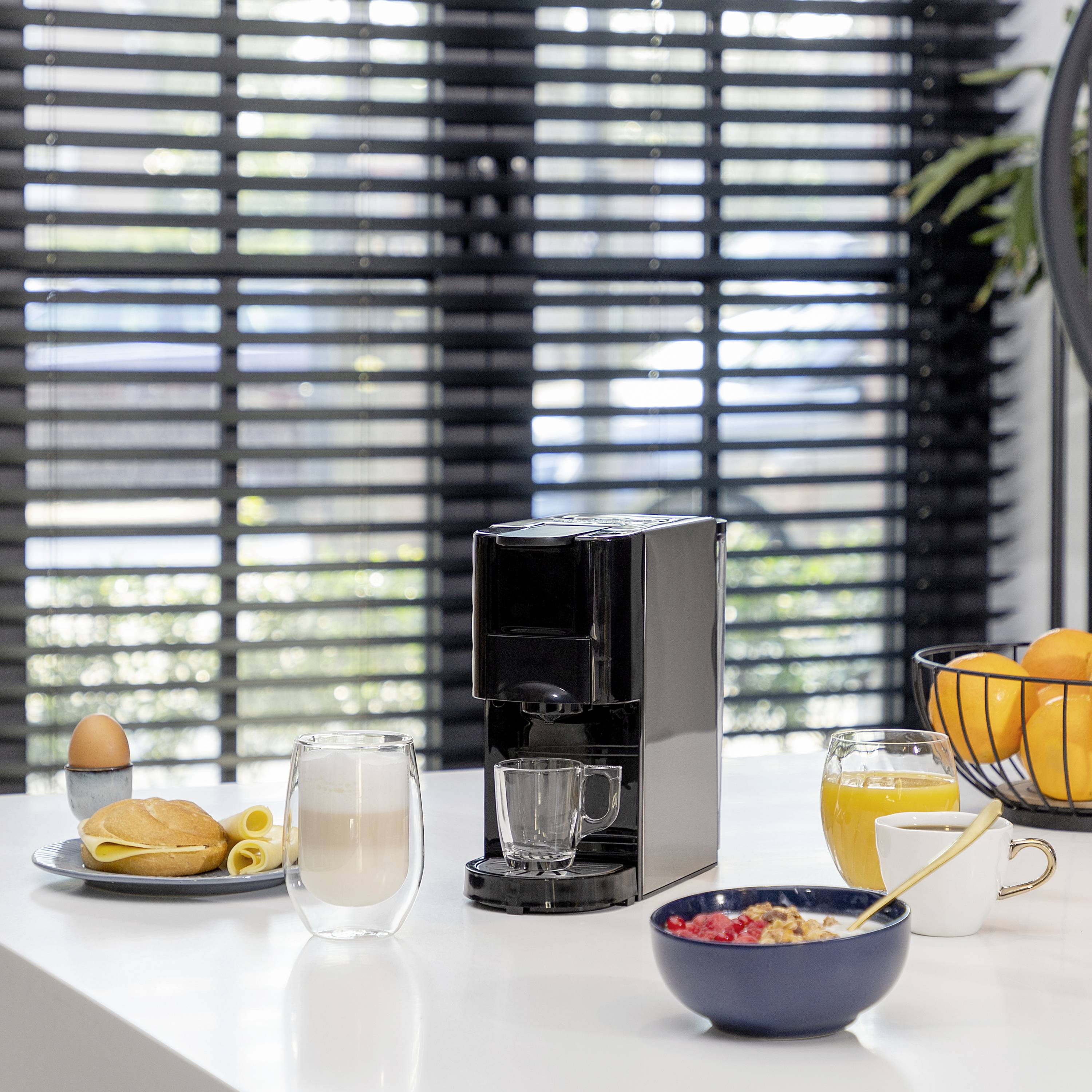 A breakfast table with a coffee machine, fresh juice, cereal, and pastries in a bright room with large slatted windows.