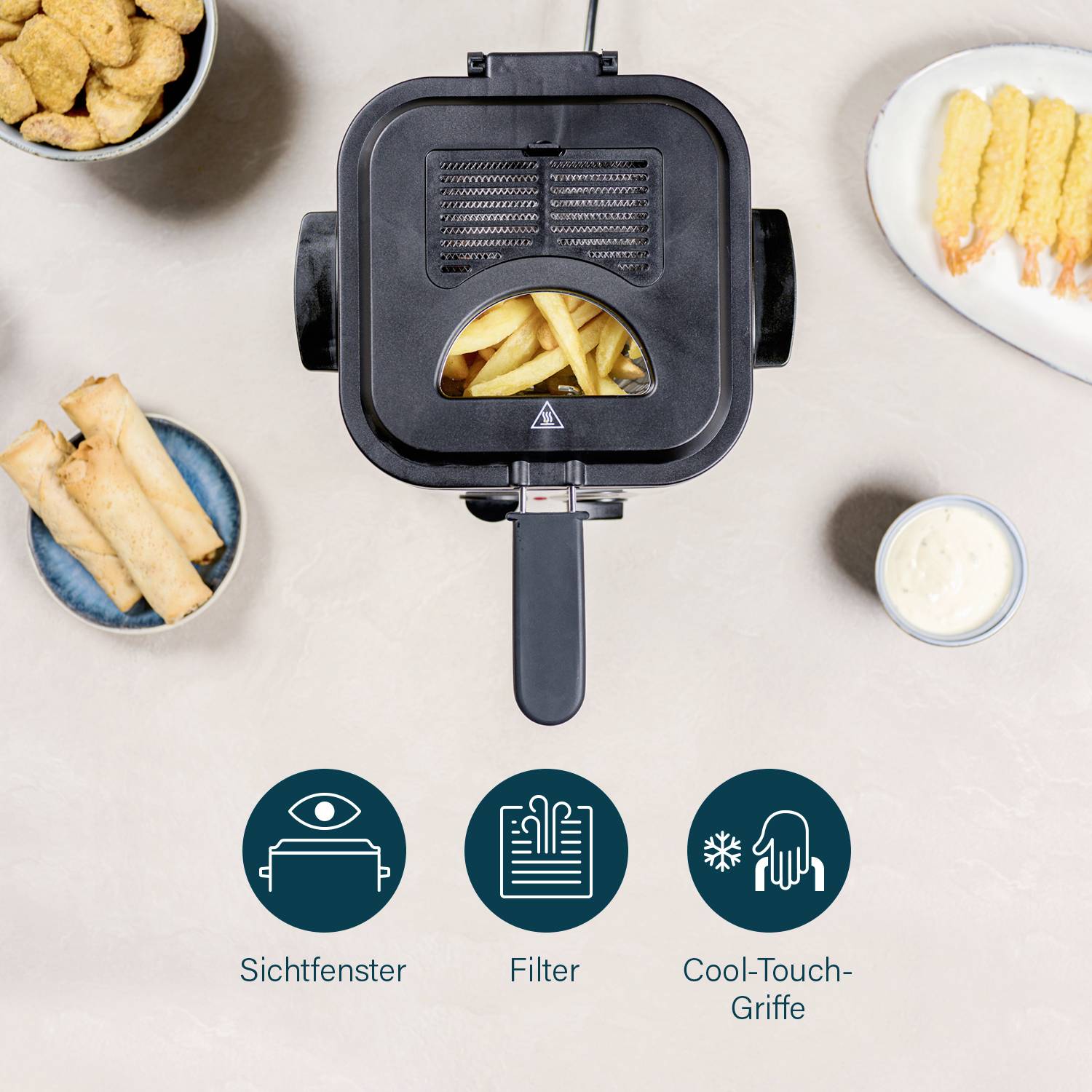 A deep fat fryer with a viewing window, filter and cool-touch handle. Beside the fryer are chips, prawns and spring rolls on plates.