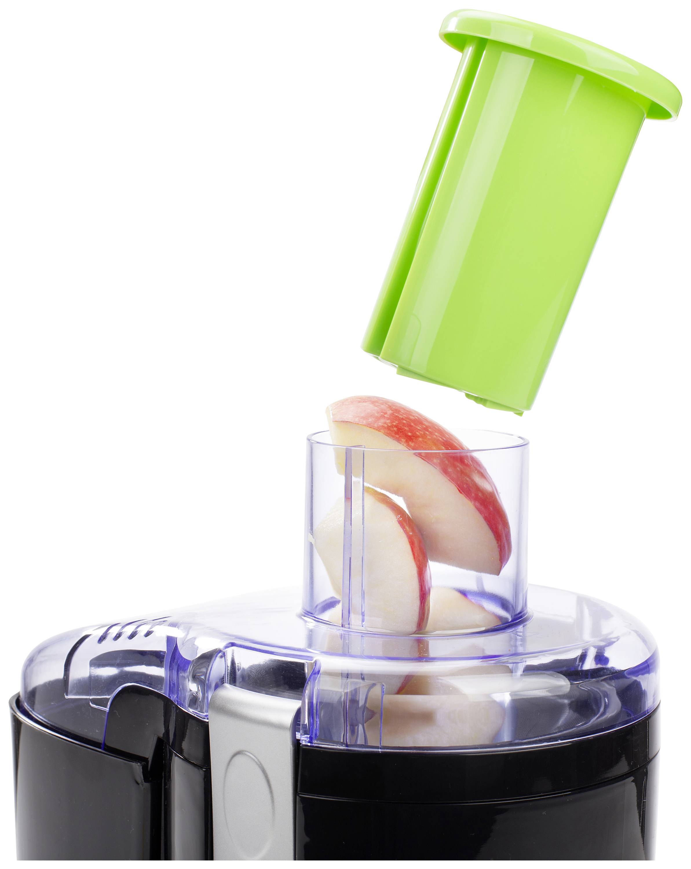A juicer with apple slices in the feed chute. A green plunger helps to push the pieces into the machine.