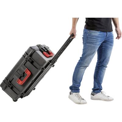 A standing person is pulling a black wheeled suitcase with a red handle across the ground.