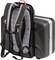 A black rucksack with grey shoulder straps is attached to the back of a black, hard suitcase.