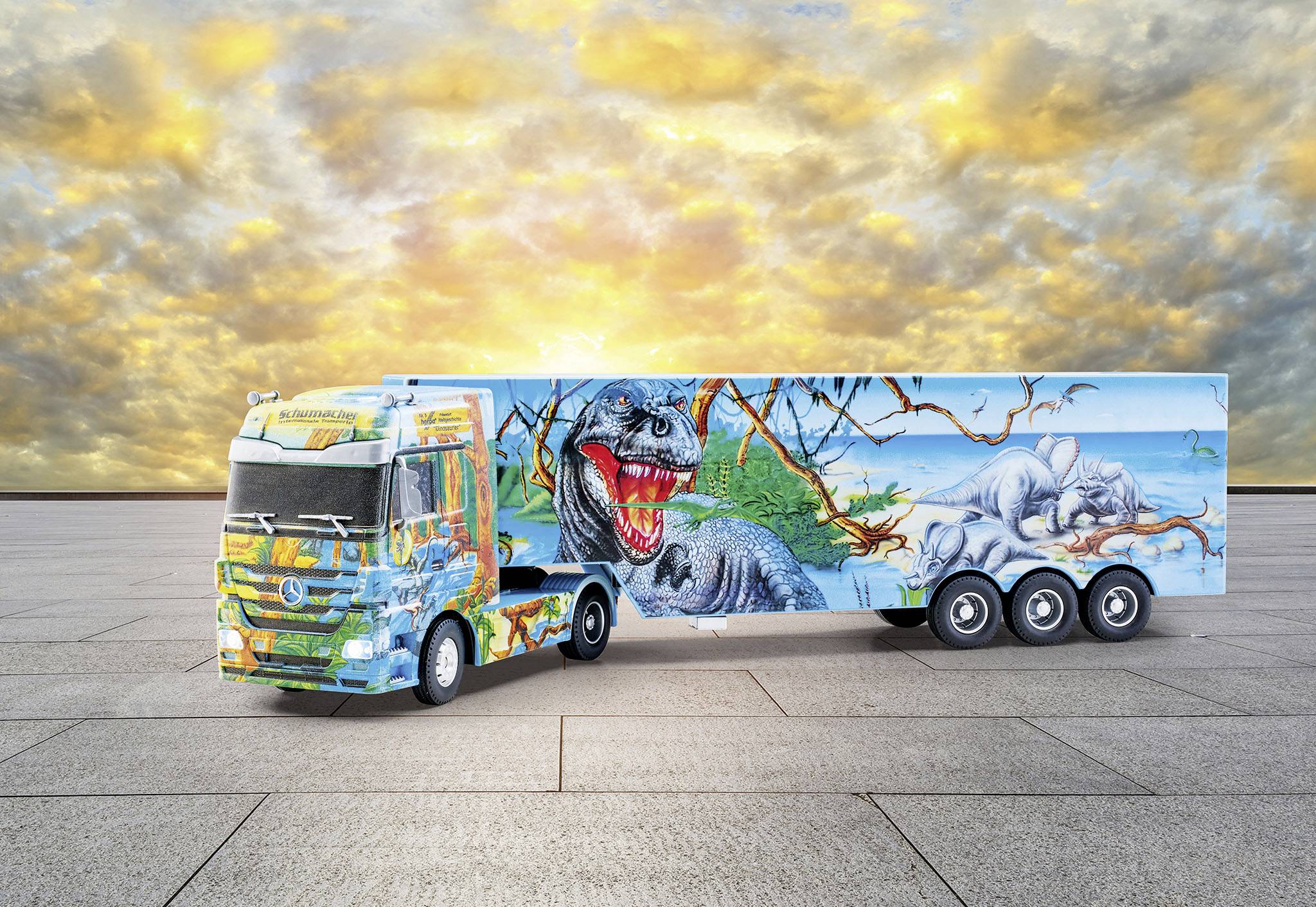 A colourful painted lorry displays dinosaurs and a landscape. In the background, a dramatic sky with clouds and sunset can be seen.