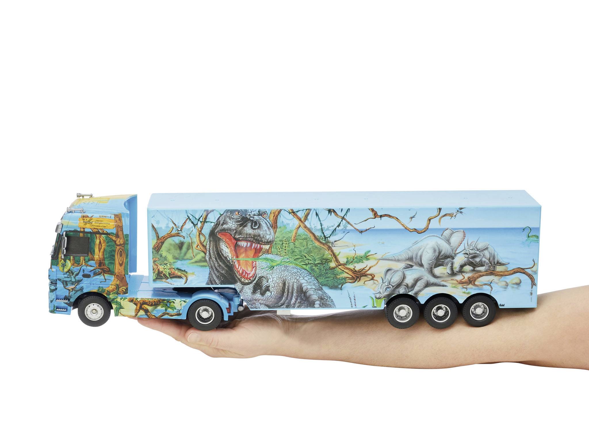 A toy lorry with dinosaur themes is being held in a hand. The trailer depicts a Tyrannosaurus and a Triceratops.