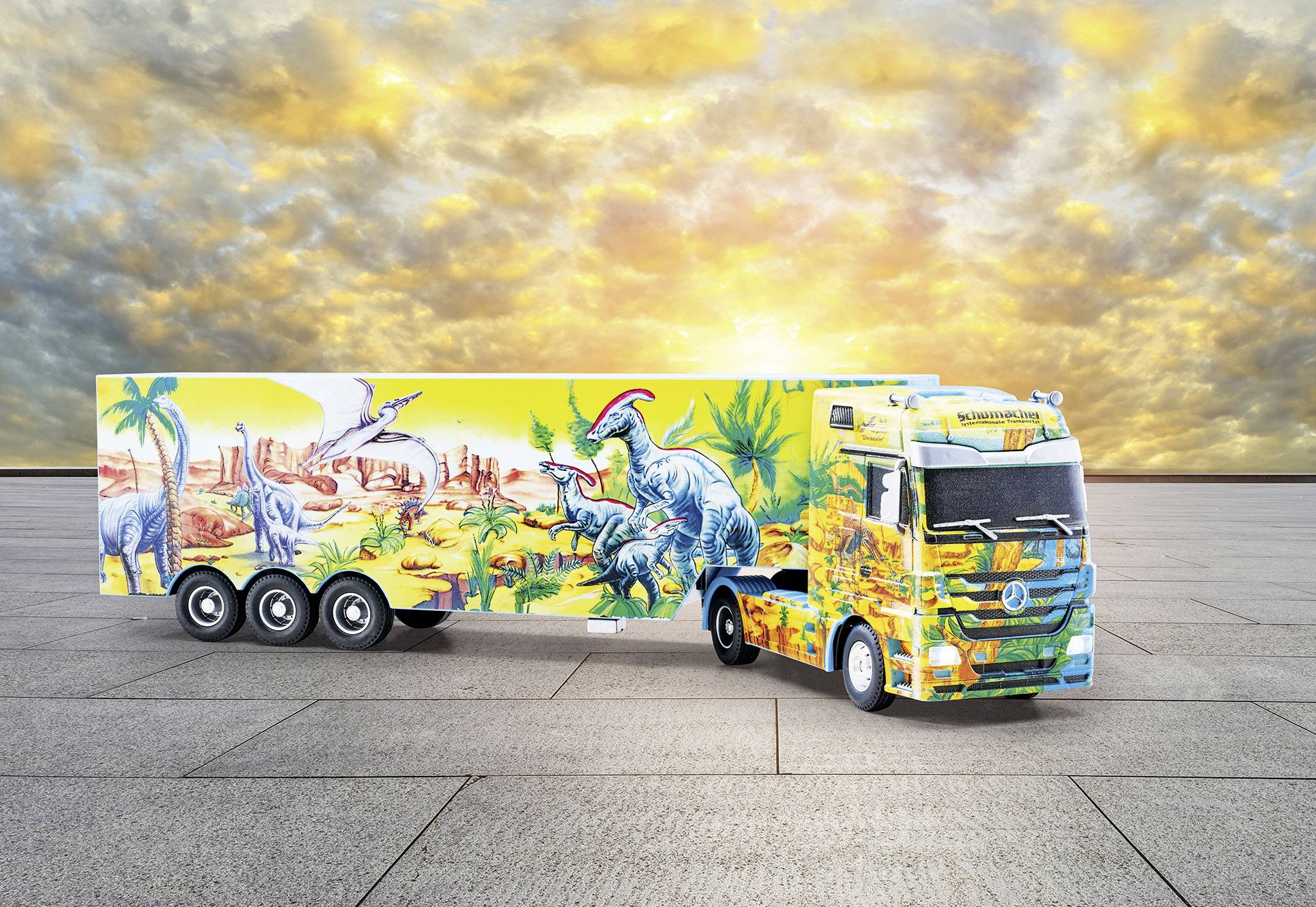 Colourful lorry with dinosaur motifs parked on a paved square at sunset.