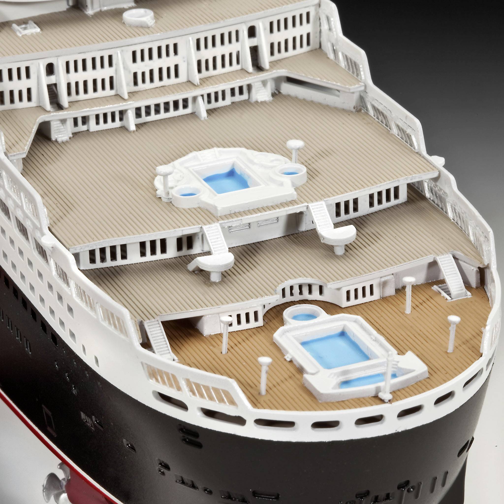 Model of a multi-storey cruise ship deck with two blue pools and white railings that emphasise the vessel's luxury.