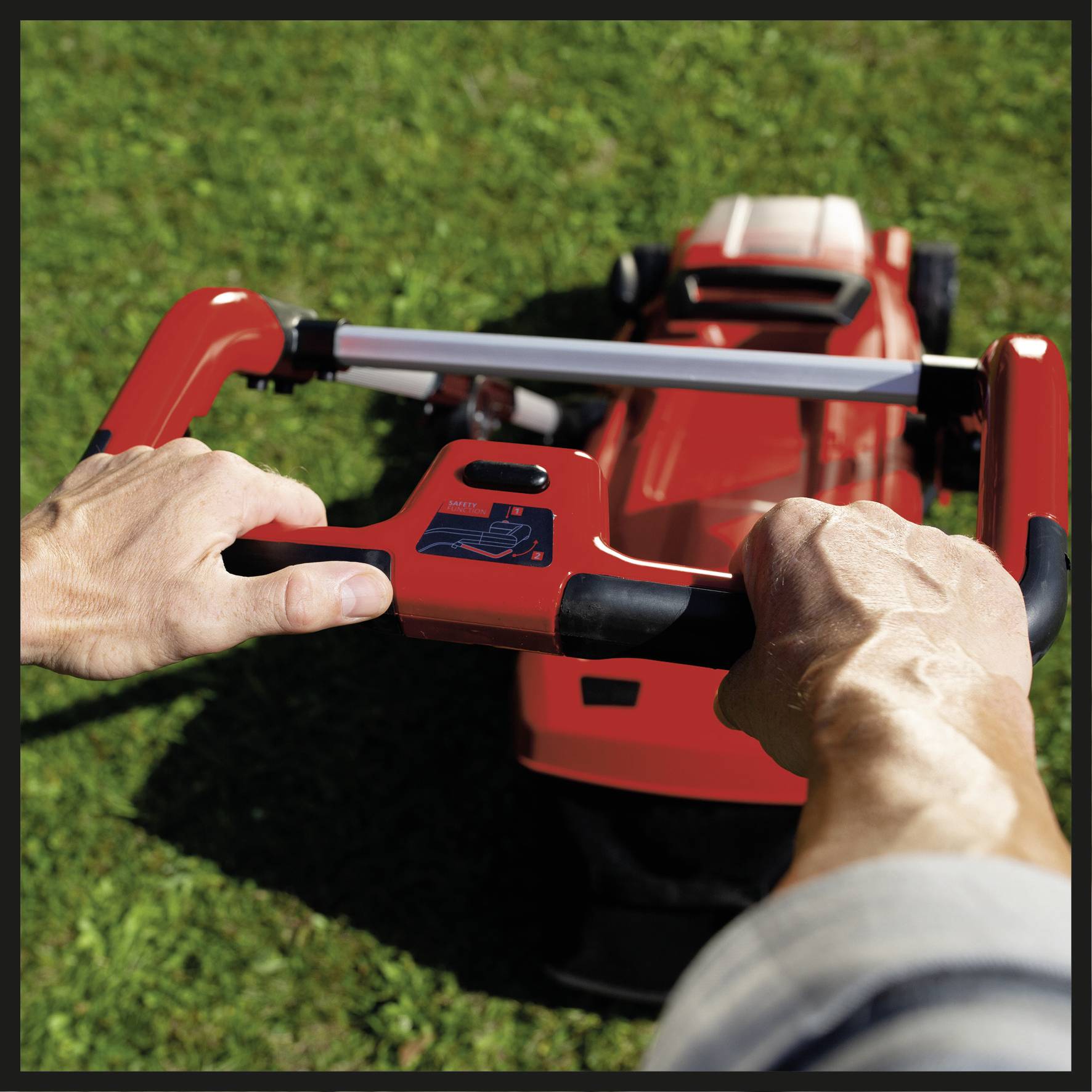 A person is pushing a red lawnmower across a green lawn. Hands are gripping the mower's handle, focused on operating the machine.
