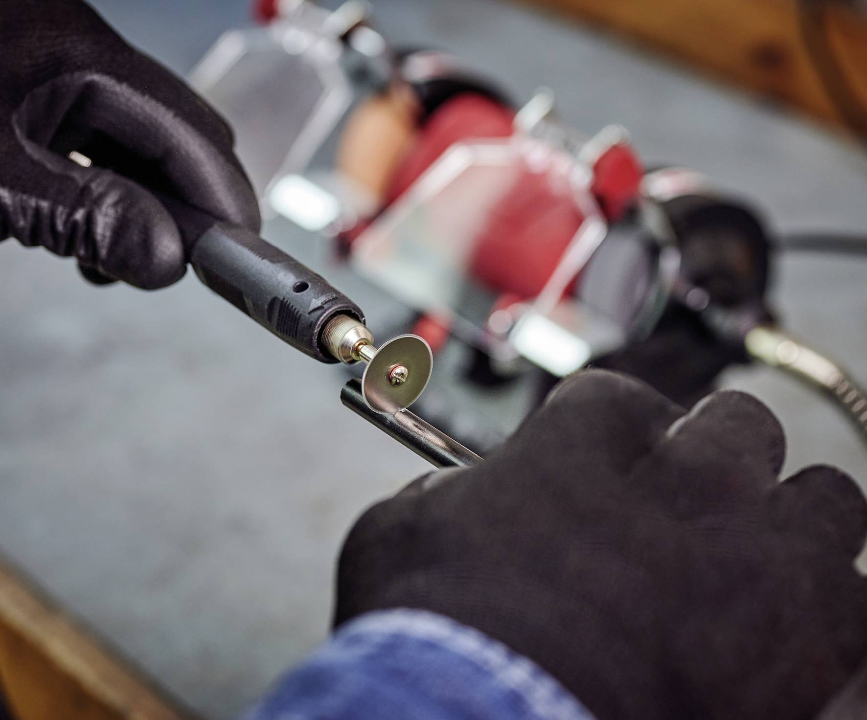 'A person is grinding a piece of metal with a rotating tool. Grinding wheel and hands in gloves are visible.'