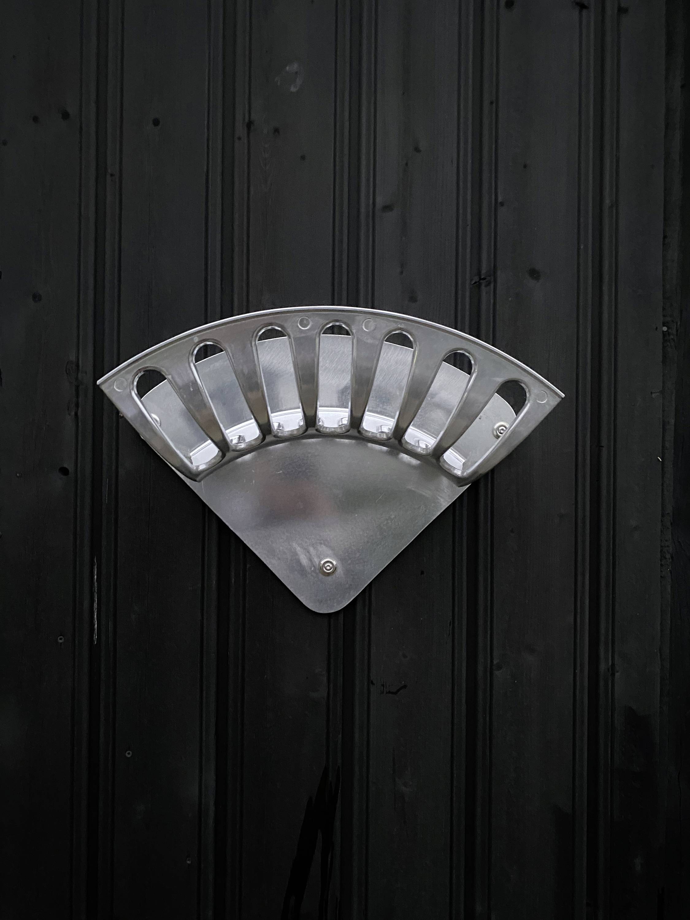 A metallic artwork in the shape of a fan against a black background, mounted on a vertical surface.