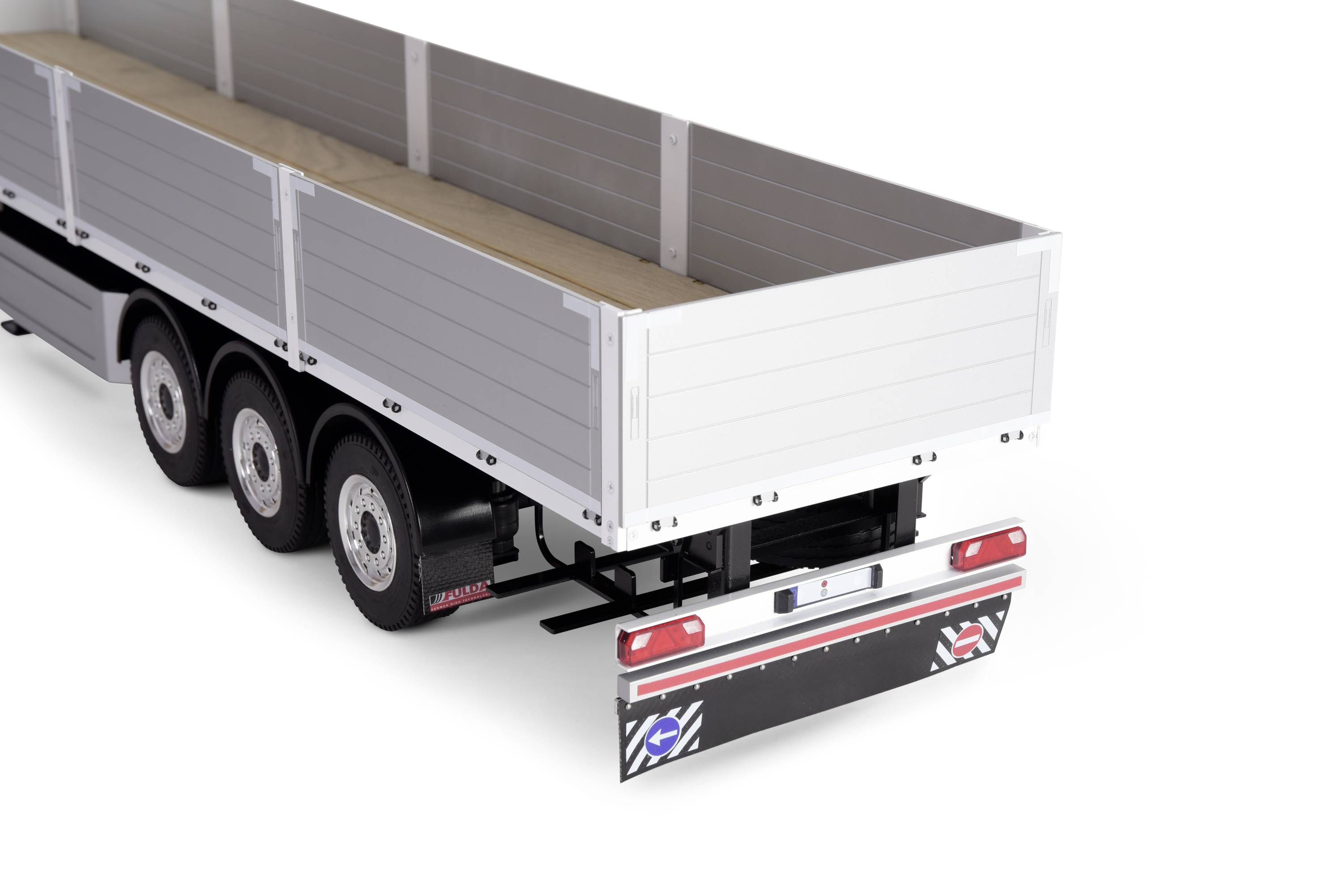 A white trailer with three axles, an open loading area, and a raised stand at the back, is standing against a white background.