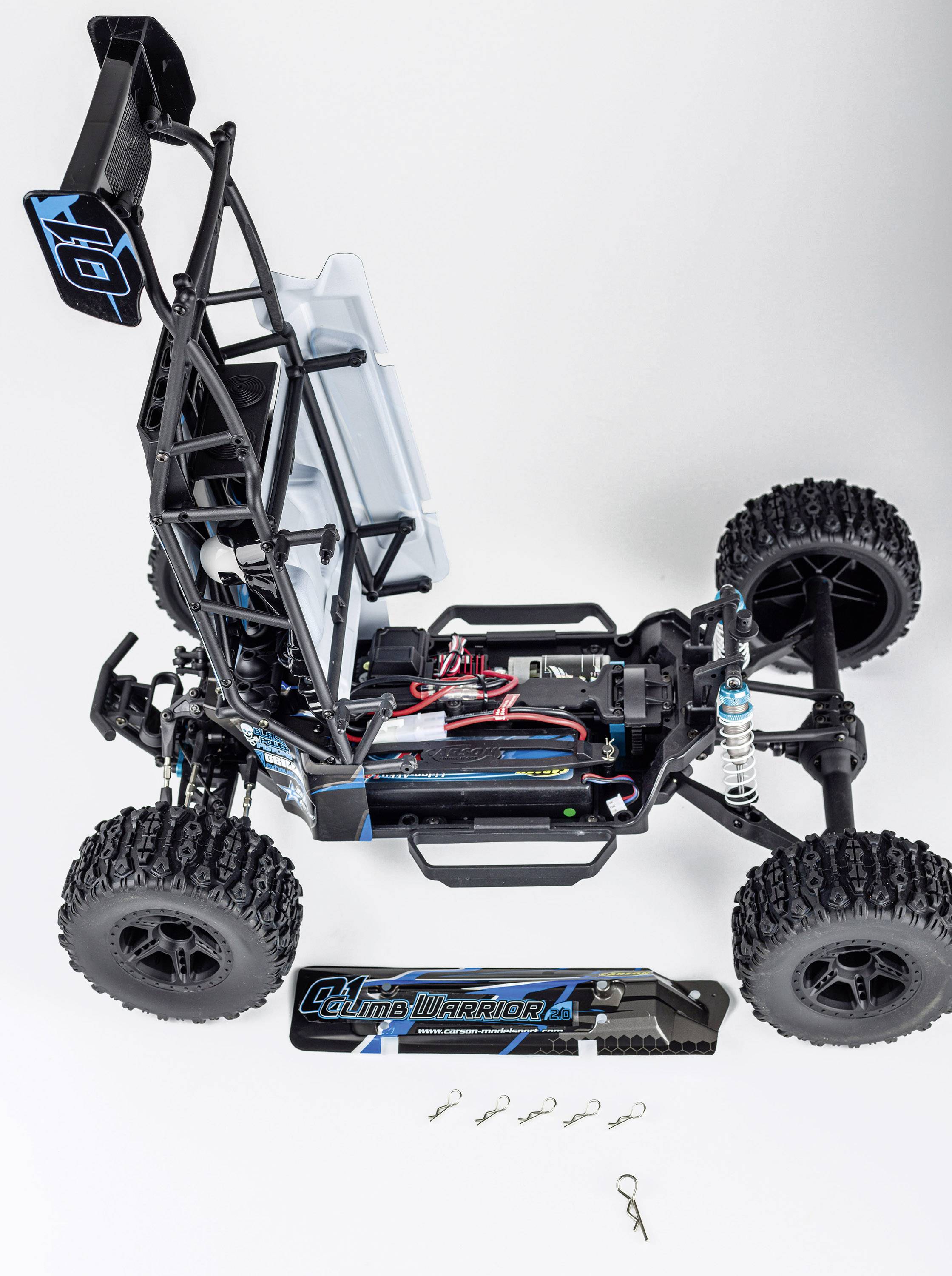 Remote-controlled car with open bodywork reveals internal structure and components. Accessories and tools are laid out in front on a white background.