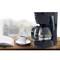 Coffee machine with glass carafe and cups on a wooden worktop, with an open book beside it; cosy kitchen scene.