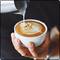 A person artfully pours frothed milk into a cup of coffee to create a heart pattern.