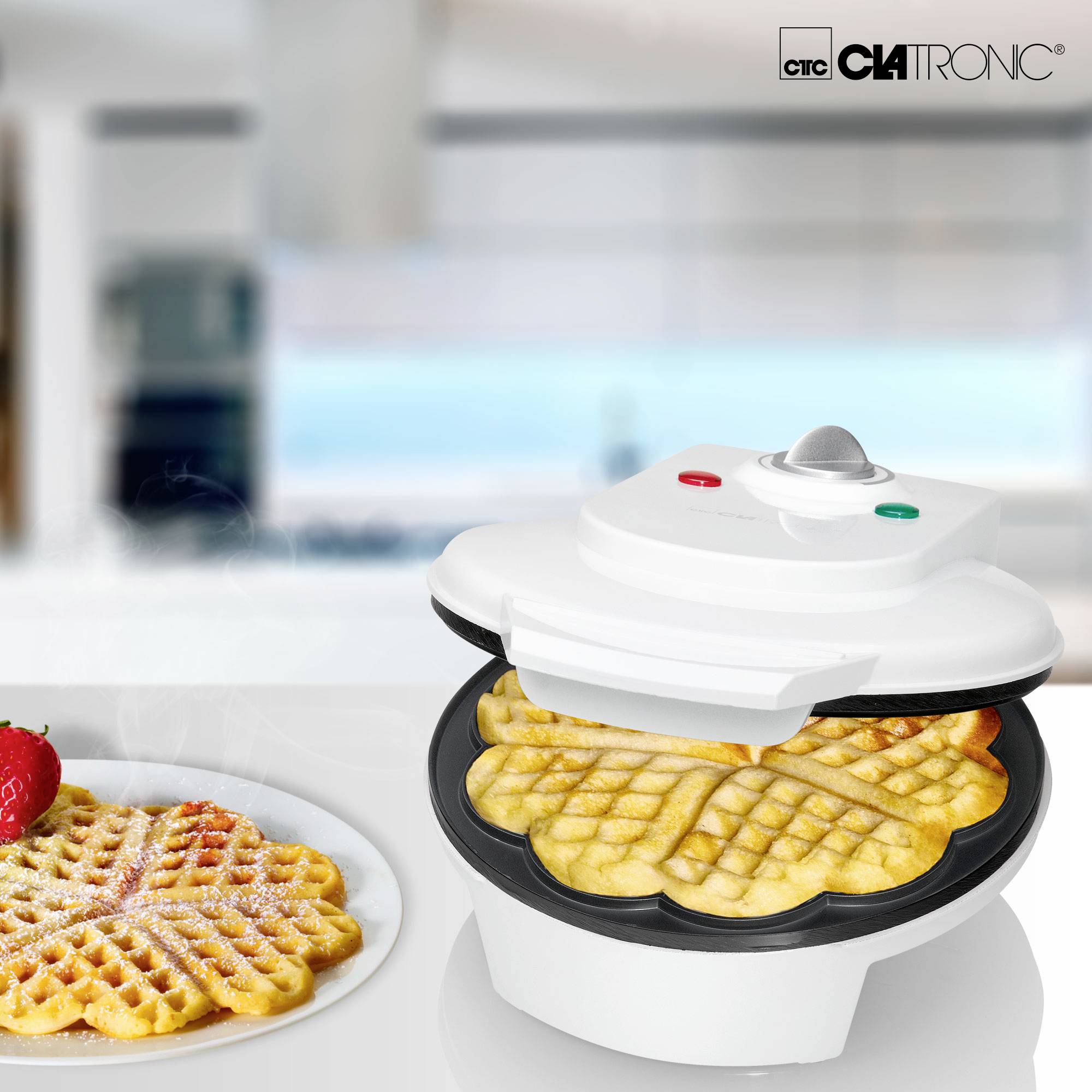 A waffle iron with freshly baked waffles, decorated with icing sugar and strawberry. In the background, a blurred kitchen view.