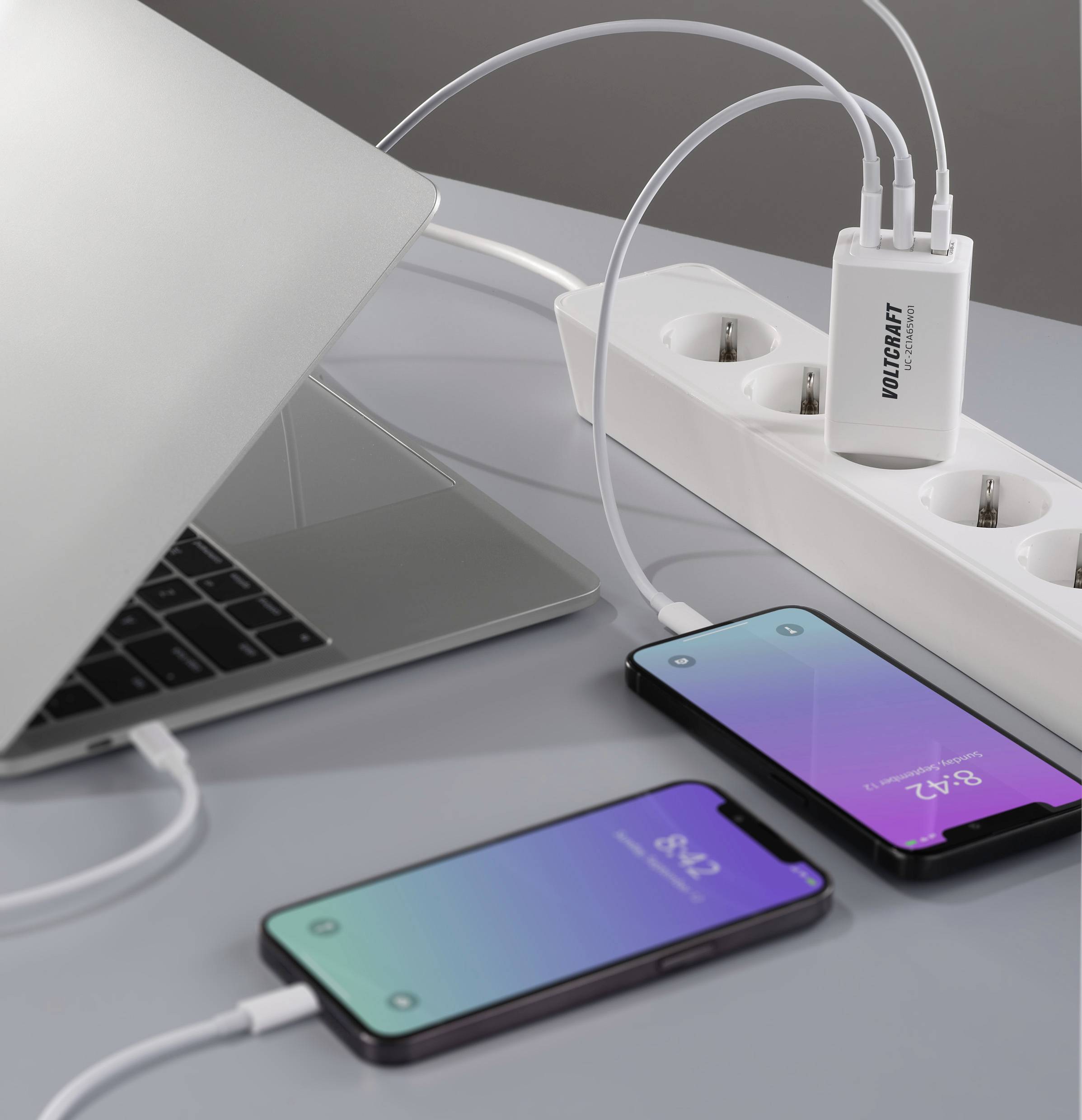 A laptop and two smartphones are being charged via a multi-socket power strip. All devices are connected to the socket by cable.