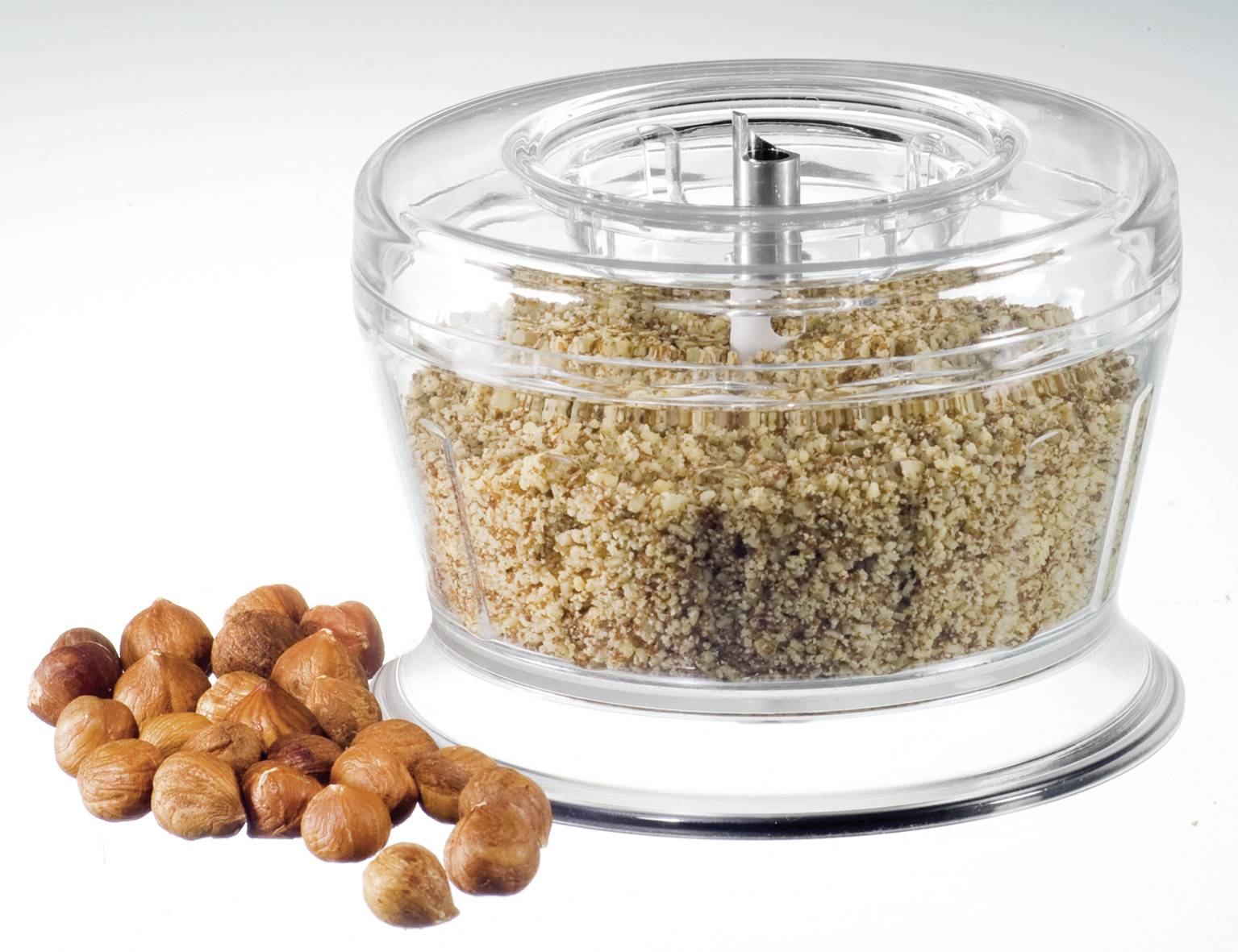 Chopped hazelnuts in a transparent container, with whole hazelnuts beside it.
