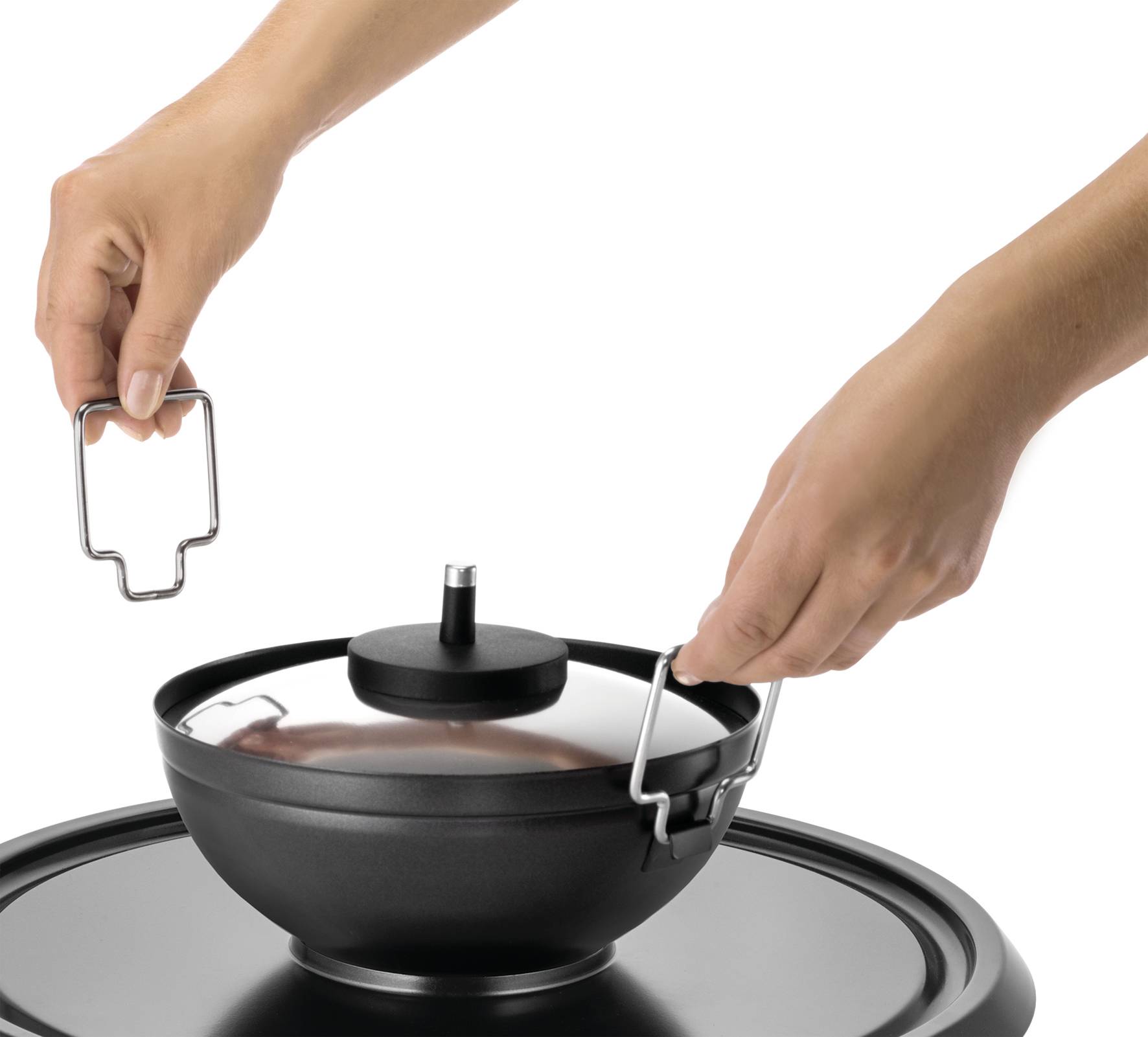 Hands are lifting a lid with a raised handle from a round black pot. The pot is sitting on a smooth, dark surface.