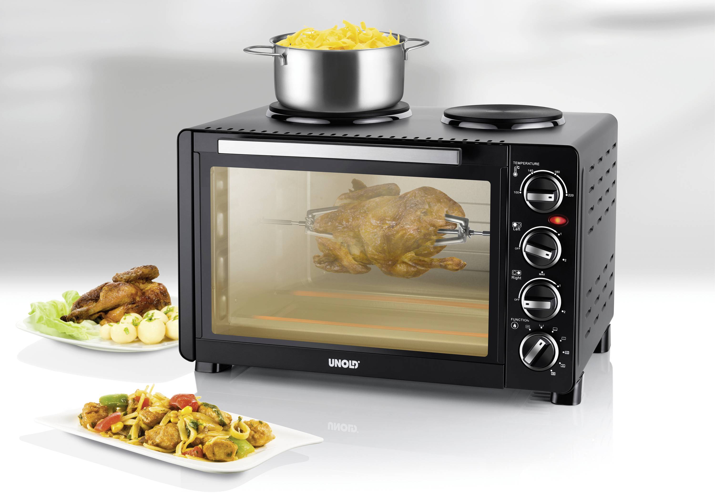 A black oven with three rotary knobs, in which a chicken is being grilled. A pot of pasta sits on the hob.